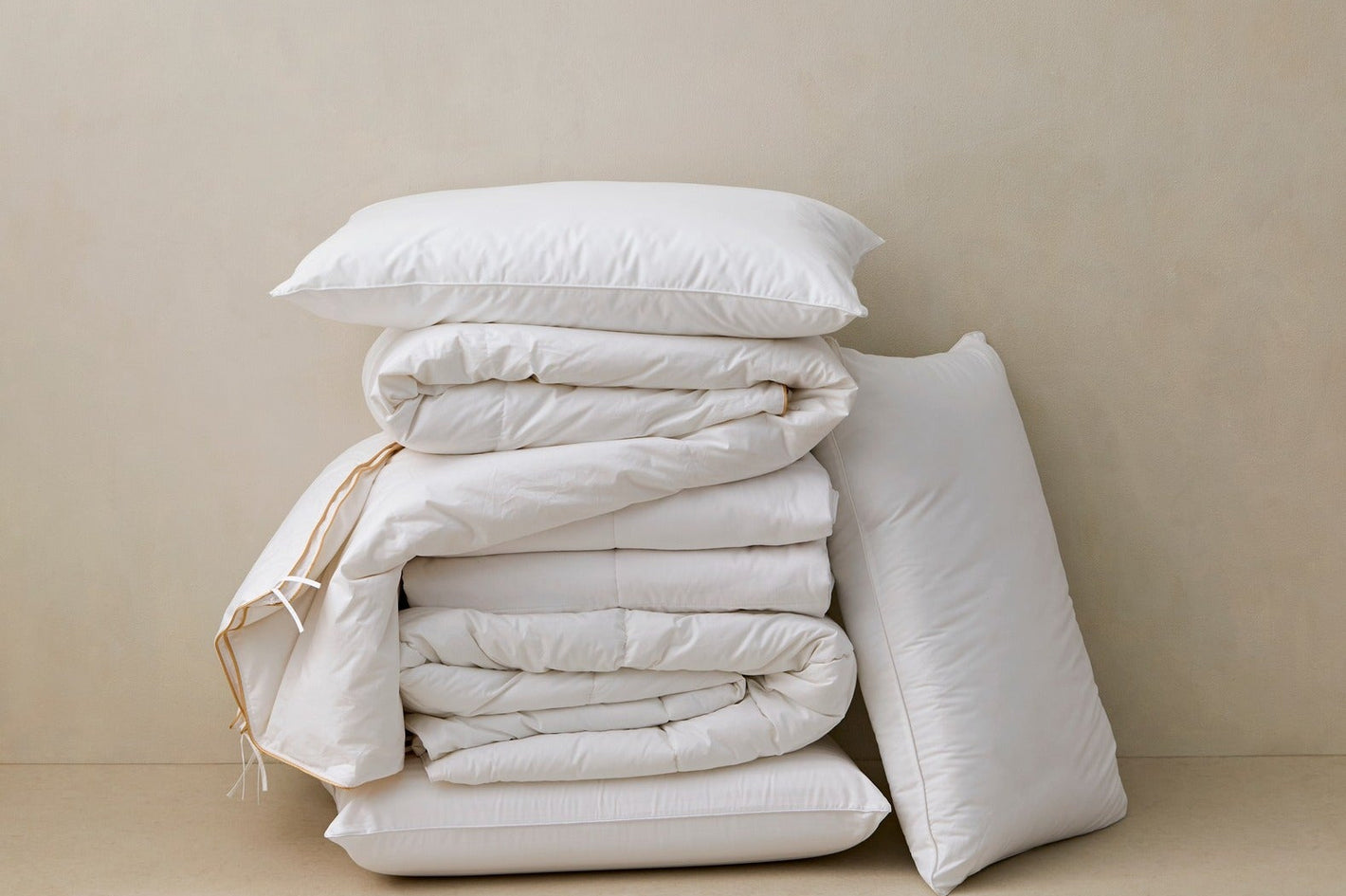 Stack of white bedding and pillows on a beige surface with a beige background